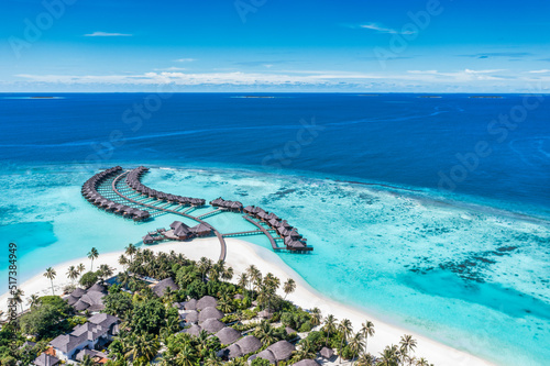 Aerial view of Maldives island, luxury travel water villas resort and wooden pier. Beautiful sky and ocean lagoon beach background. Summer vacation holiday. Paradise aerial landscape panorama