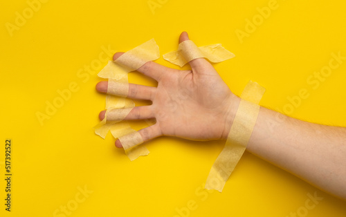 Hand sealed with masking tape isolated on yellow background with copy space. Concept of immobilized helpless human person without freedom living in the world with tabboo