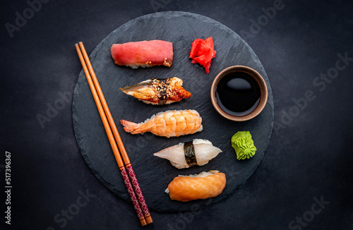 Tasty sushi sashimi set composition with shrimps, ginger and soy sauce served with chopsticks and green wasabi on black plate on table from above. Traditional asian food with rice and seafood