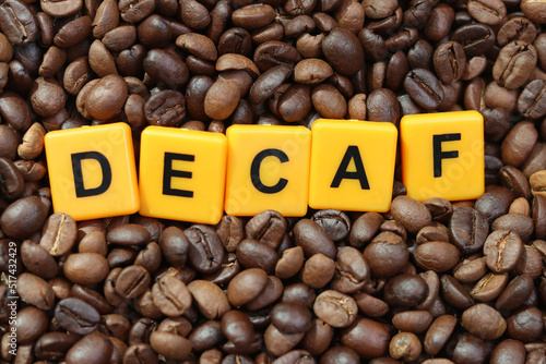 Decaf word on roasted coffee beans background. Concept of decaffeinated coffee or low caffeine coffee.