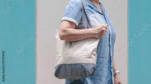 Midsection of plus size woman carrying reusable canvas eco friendly tote bag on pastel blue and gray wall outside of supermarket