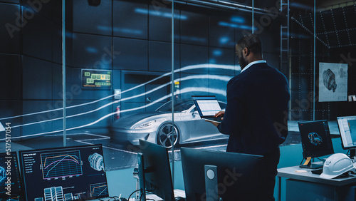 Engineering Research Agency Perform Aerodynamic Testing with a Modern Eco-Friendly Electric Sports Car in a Wind Tunnel. Professional Scientist Works on a Laptop Computer and Changes Testing Options.