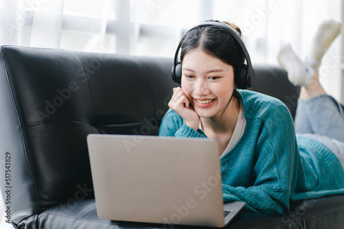 Smart and positive Asian female freelancer or female college student sitting on sofa with laptop. Study from online webinars or home courses. Video calling and chatting