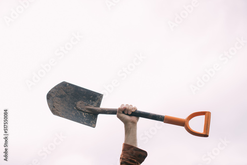 A man's hand holds a bayonet shovel on a white background. Metal shovel in his hands against the sky