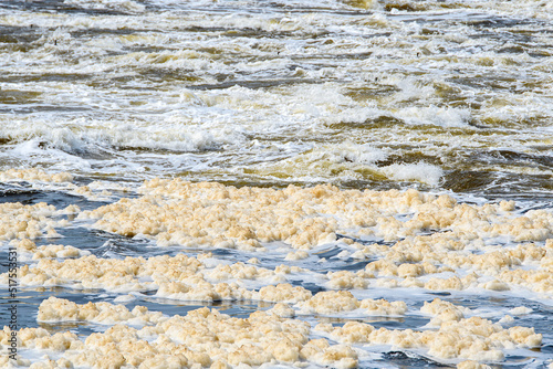 A fast flowing river filled with dirty pollution foam. The foam is a light dirty brown. Shallow depth of field.