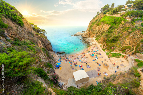 Tourists and local Spanish enjoy a summer sunset at Cala Codolar, a small sandy beach cove at the Costa Brava town of Tossa de Mar, Spain, on the Mediterranean Sea.