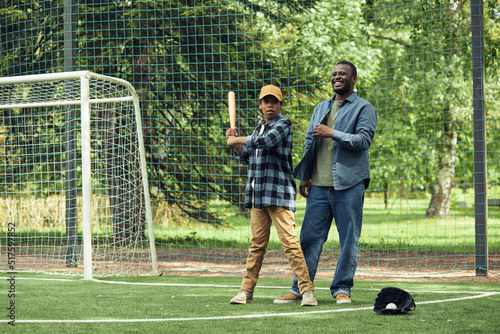 African happy dad learning his son to play baseball on the field outdoors