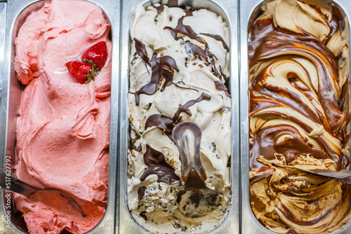 Tre vaschette di gelato artigianale al gusto fragola, stracciatella e tiramisù nella vetrina di una gelateria artigianale pronte per essere vendute