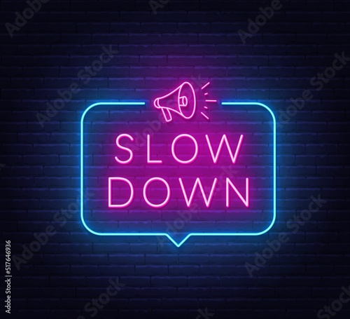 Slow Down neon sign in the speech bubble on brick wall background.