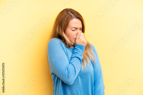 blonde pretty woman feeling disgusted, holding nose to avoid smelling a foul and unpleasant stench