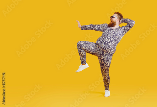 Funny fat fashion guy in pajamas posing on copy space background. Full length portrait of happy joyful plump bearded young man wearing crazy leopard PJs dancing on blank yellow copyspace background