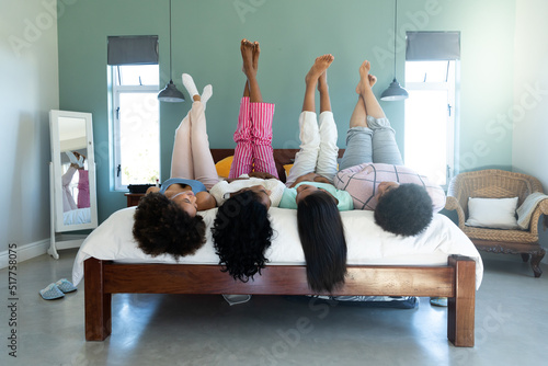 Biracial carefree young biracial friends with feet up lying by side by side on bed against wall