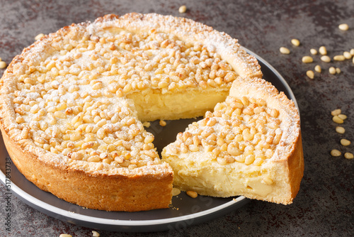 Torta della Nonna is the most delicious Italian custard tart made with sweet shortcrust pastry, custard cream and topped with pine nuts closeup in the plate on the table. Horizontal