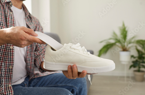 Young man puts new clean orthotic insole with foot arch support inside modern white comfortable orthopedic shoe he is holding in his hand. Cropped shot. Pain treatment and flatfoot prevention concept