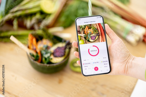 Holding smart phone with running mobile application for track calories consumed on background of healthy food ingredients. Concept of modern technology in proper nutrition