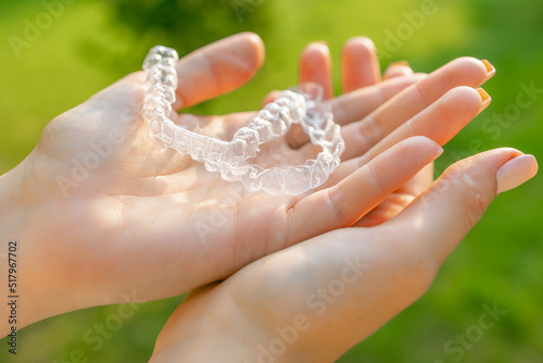 Close up womans hand holding invisible aligners for whitening and straightening of teeth on the green background. Orthodontic therapy after brackets. Teeth healthcare
