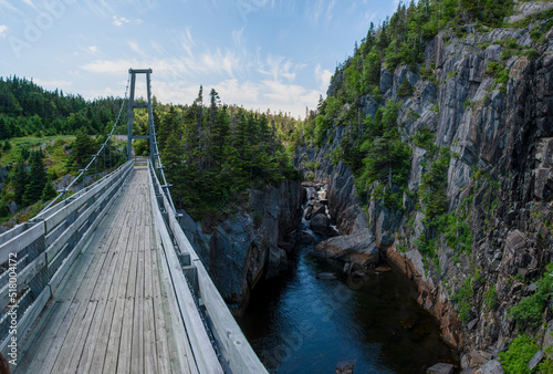 The reconstructed suspension bridge of the ghost town of La Manche, Newfoundland crosses over the cove beside a small waterfall, connecting the East Coast Trail.