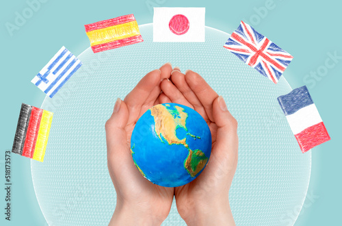 International interpreter. Woman's hands hold a small globe of the planet Earth, close-up. Light blue background with a digital sphere and flags. Concept of linguistics and learning foreign languages