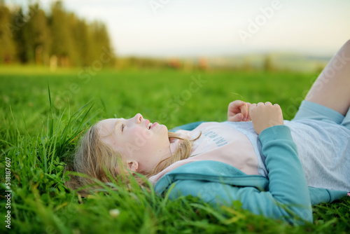 Cute young girl having fun outdoors on sunny summer day. Child exploring nature. High mountains and green hills in summer or spring.