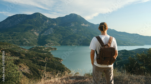 Back view of wanderlust man with backpack looking at scenic view of lake and mountains from a view point.