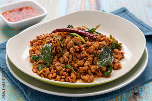 Spicy duck pad kra pao or pad kra pao ped, minced duck stir-fried with holy basil leaves, ground dried chilis and chopped garlic cloves to create this savory Thai dish, served on a beige-white plate.