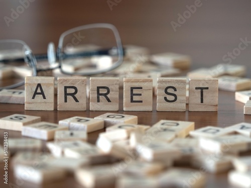 arrest word or concept represented by wooden letter tiles on a wooden table with glasses and a book