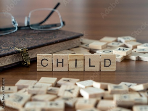child word or concept represented by wooden letter tiles on a wooden table with glasses and a book