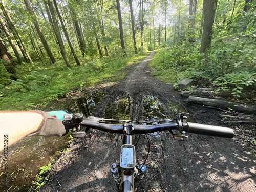 POV photo of riding a bicycle on the forest muddy path. Close up of a bike handlebar with a forest background. Concept of extremely rural and outdoor bike riding.