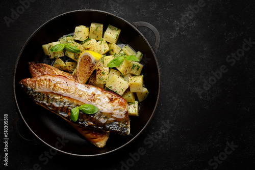Grilled mackerel fish fillet, in a pan with boiled potatoes, on a dark background