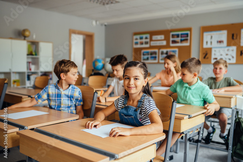 Children in the classroom at the lesson. Young cute hispanic girl looking at the camera. Classmates doing test tasks at school.