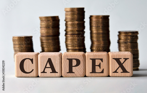 CAPEX - acronym on wooden cubes on the background of stacks of coins