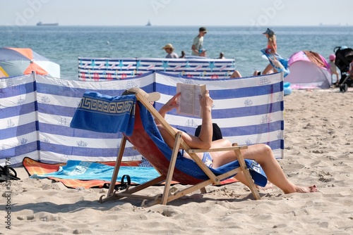 A man sits on a deck chair on the beach on a hot day, sunbathing and reading a book. Beach on the Baltic Sea in Gdansk, Poland