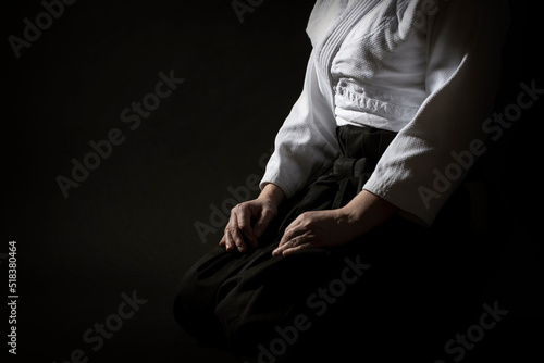 Aikido sitting pose in hakama uniform on black background. Shallow depth of field. SDF.