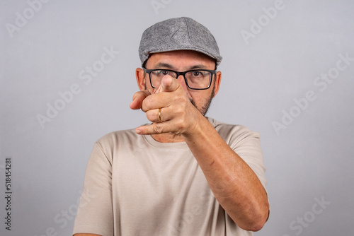 Portrait of mature businessman wearing eyeglasses over gray background. Senior brazilian man 60 years old pointing at camera isolated.
