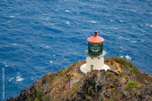 View of red and white lighthouse on cliff near beach in Oahu