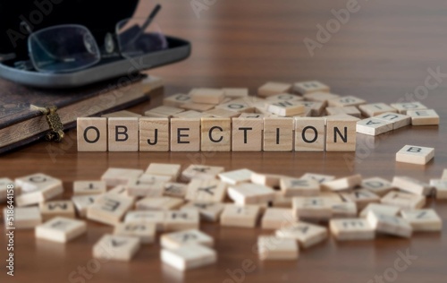 objection word or concept represented by wooden letter tiles on a wooden table with glasses and a book