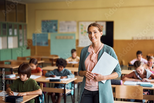 Happy elementary school teacher in classroom looking at camera.