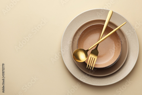 Stylish empty dishware and cutlery on beige background, top view. Space for text