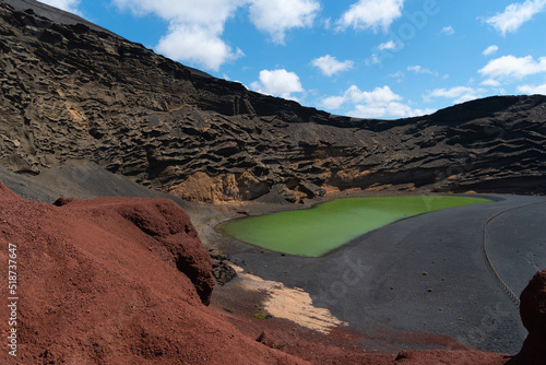Laguna de los Clicos o Charco Verde rodeado de rocas y tierra volcánicas y arena negra en Lanzarote, Islas Canarias, un día soleado con el cielo azul despejado. Recursos turísticos y naturales