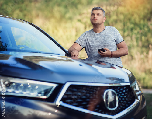 A middle-aged man is standing near the car. Muccina speaks on the phone. Dear beautiful car. The man is calm and confident. The car is in the summer park.