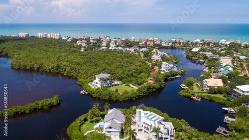 Aerial Drone Perspective of Real Estate in Bonita Springs, Florida with the Bay and a Preserve in the Foreground and the Gulf of Mexico in the Background Featuring a Blue Sky and Blue Water