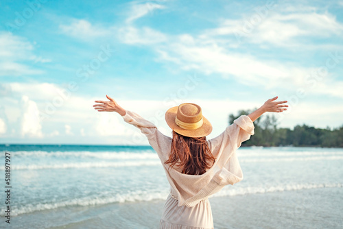 Summer beach vacation concept, Young woman with hat relaxing with her arms raised to her head enjoying looking view of beach ocean on hot summer day, copy space.