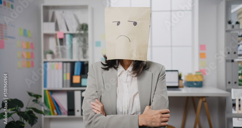 Young Asian businesswoman sit on desk wear draw sad mask paper craft bag feel bad mood with fail work project at office. Anonymous young lady mad and confuse with overwork, Work mental health.