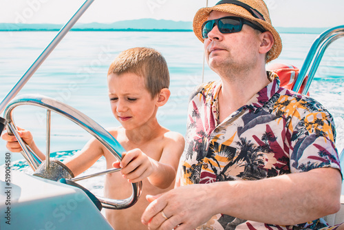 Son and father driving motorboat on holiday. Men teaching a young boy sailing an inflatable rubber motor boat on the sea. Boat rental