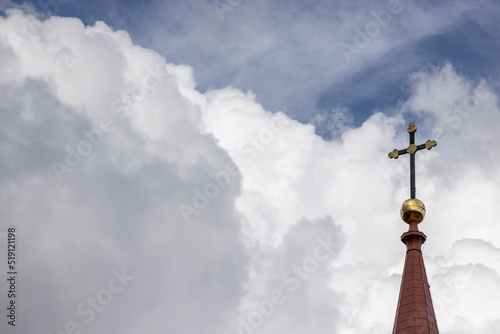 Tower of the roof of a lutheran church with a cross on the very top with beautiful thick clouds in the background Nr.2