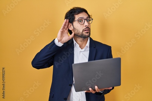 Handsome latin man working using computer laptop smiling with hand over ear listening an hearing to rumor or gossip. deafness concept.