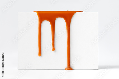 Dripping caramel drops of sweet caramel sauce on white podium on white background. Melted caramel sauce drip, drops of sweet liquid toffee.