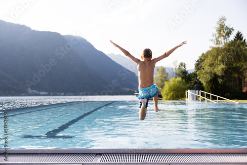 Active teenager boy jumping into an outdoor pool in the Alps. Summer holiday concept