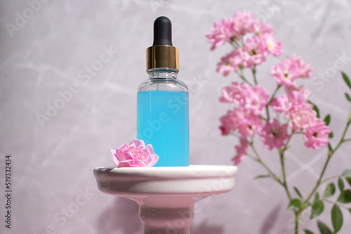 Glass dropper bottle on podium with flowers on marble background. Cosmetic container mock-up.