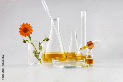 bottle with a pipette, laboratory flasks and calendula flowers on a gray background